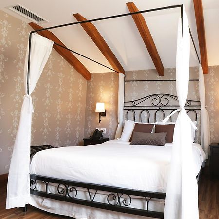 Buona Vitta Gramado Resort & Spa By Gramado Parks Exterior foto The photo shows a beautifully designed bedroom featuring a four-poster bed with a metal frame and flowing white curtains. The bed is adorned with white bedding and brown decorative pillows. The room has wooden beams on the ceiling and is decorated wi