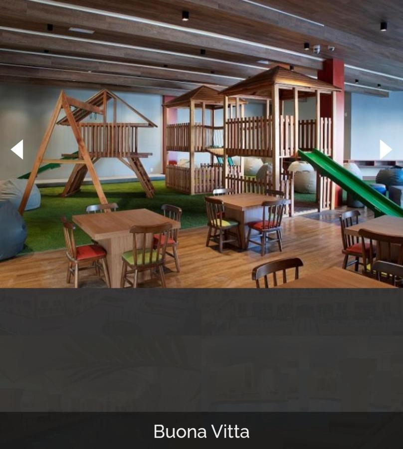 Buona Vitta Gramado Resort & Spa By Gramado Parks Exterior foto The photo shows a play area designed for children, featuring a wooden play structure with slides and climbing areas. In the foreground, there are several small wooden tables and chairs arranged for seating. The floor is covered with green turf, resem