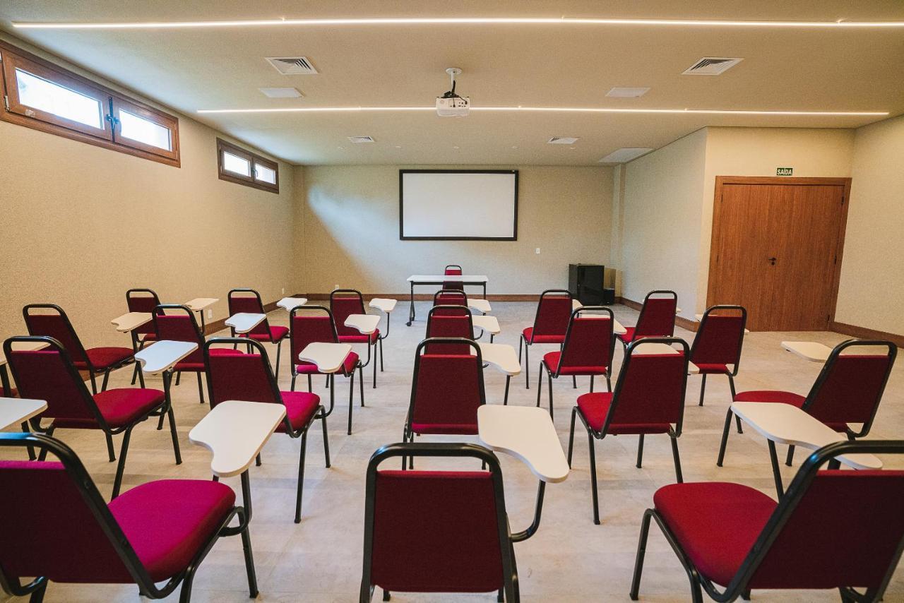 Buona Vitta Gramado Resort & Spa By Gramado Parks Exterior foto The photo shows a classroom or meeting room set up for a presentation or lecture. It features several rows of red chairs, each with a small writing surface attached. There is a blank screen mounted on the wall at the front of the room, likely for dis