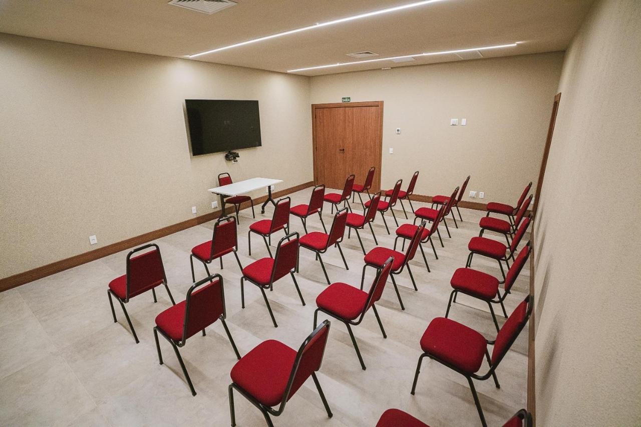 Buona Vitta Gramado Resort & Spa By Gramado Parks Exterior foto The photo shows a conference or meeting room with a simple and modern design. There are several rows of red chairs arranged in a semi-circle facing a white table at the front. On the wall opposite the chairs, there is a flat-screen television mounted