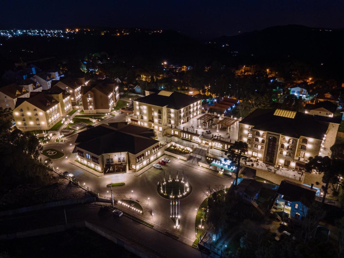 Buona Vitta Gramado Resort & Spa By Gramado Parks Exterior foto The photo shows a beautifully lit resort or hotel complex taken at night. The buildings are well-illuminated, highlighting their architecture. There is a circular area with a fountain at the center, surrounded by pathways that connect various parts o