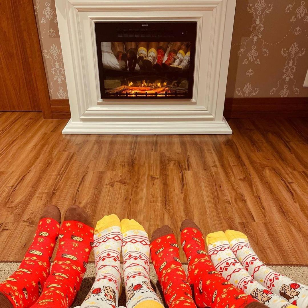 Buona Vitta Gramado Resort & Spa By Gramado Parks Exterior foto The photo shows a cozy indoor setting with a warm fireplace. In the foreground, several pairs of feet are displayed, each wearing brightly colored socks with various patterns. The socks include red, yellow, and white designs, contributing to a cheerf