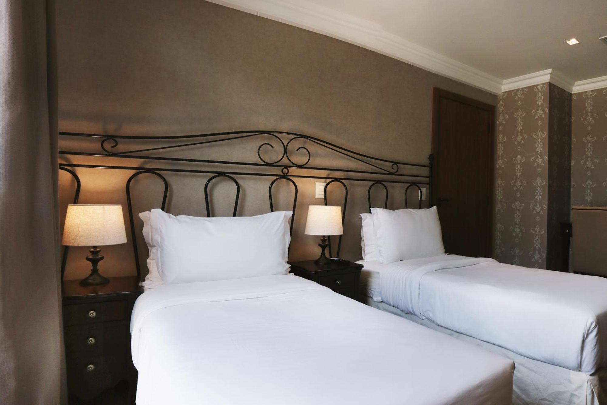 Buona Vitta Gramado Resort & Spa By Gramado Parks Exterior foto The photo shows a neatly arranged hotel room featuring two single beds with white bedding. The beds have decorative metal headboards, and there are bedside tables on either side with lamps. The room's walls have a subtle design, and there is a door v