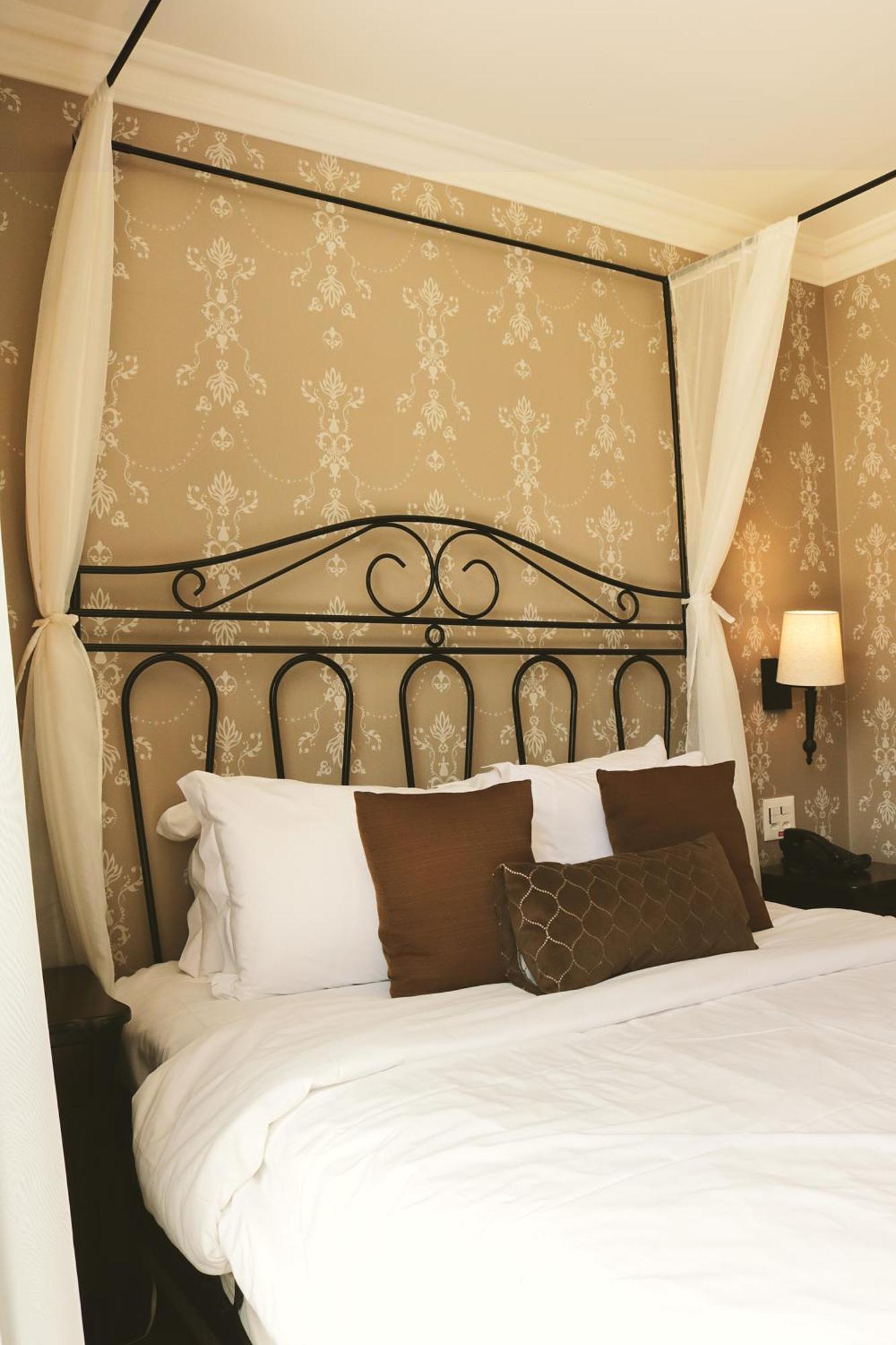 Buona Vitta Gramado Resort & Spa By Gramado Parks Exterior foto The photo shows a cozy bedroom setup featuring a decorative metal bed frame with a scroll design as the headboard. The bed is adorned with several white pillows and two brown decorative cushions. The wall behind the bed is covered with a light-colore