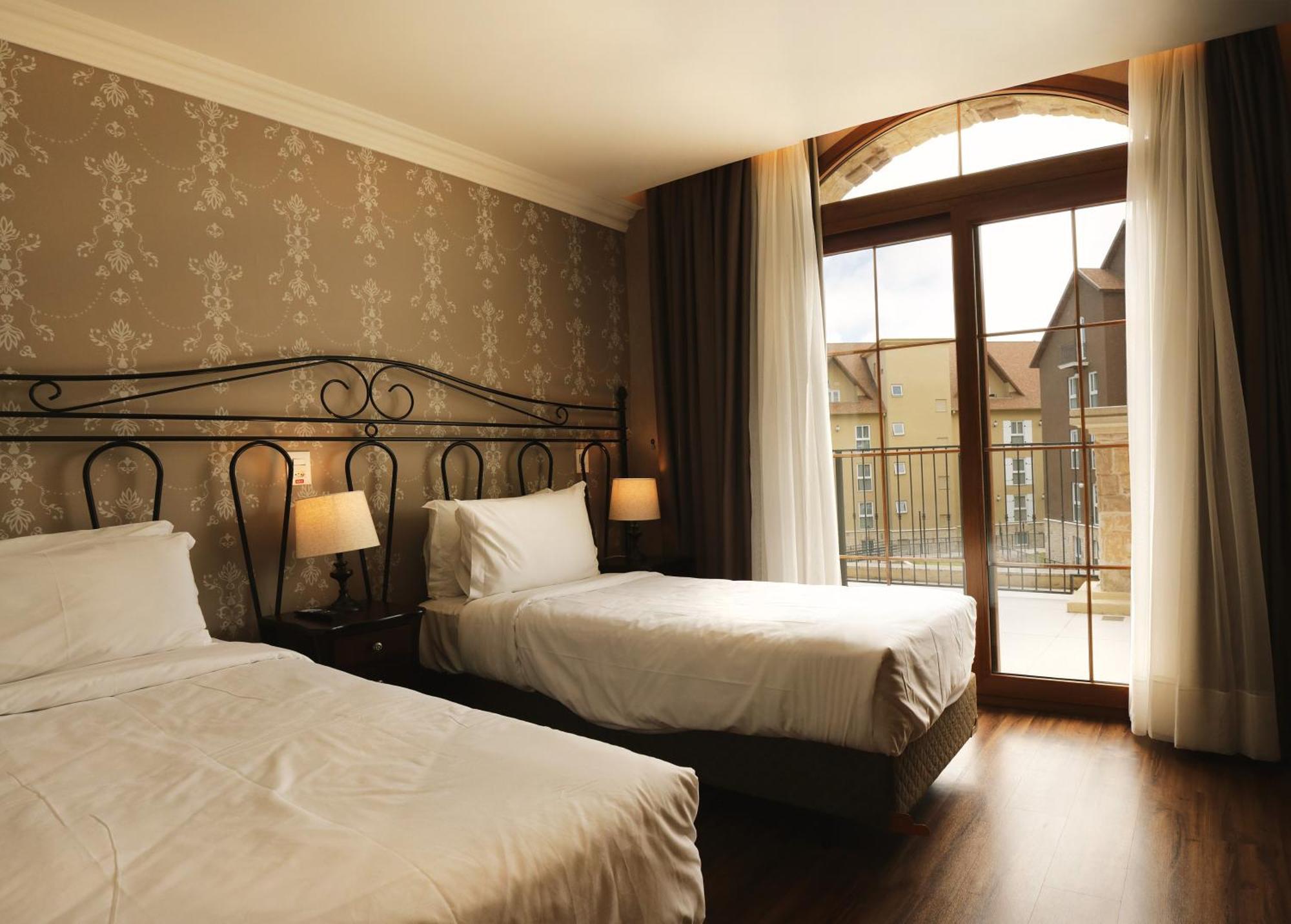 Buona Vitta Gramado Resort & Spa By Gramado Parks Exterior foto The photo shows a well-decorated hotel room featuring two beds. One bed is larger, likely a double bed, while the other is a single bed. The walls are adorned with a floral pattern, and there are bedside lamps next to the larger bed. Large windows wi