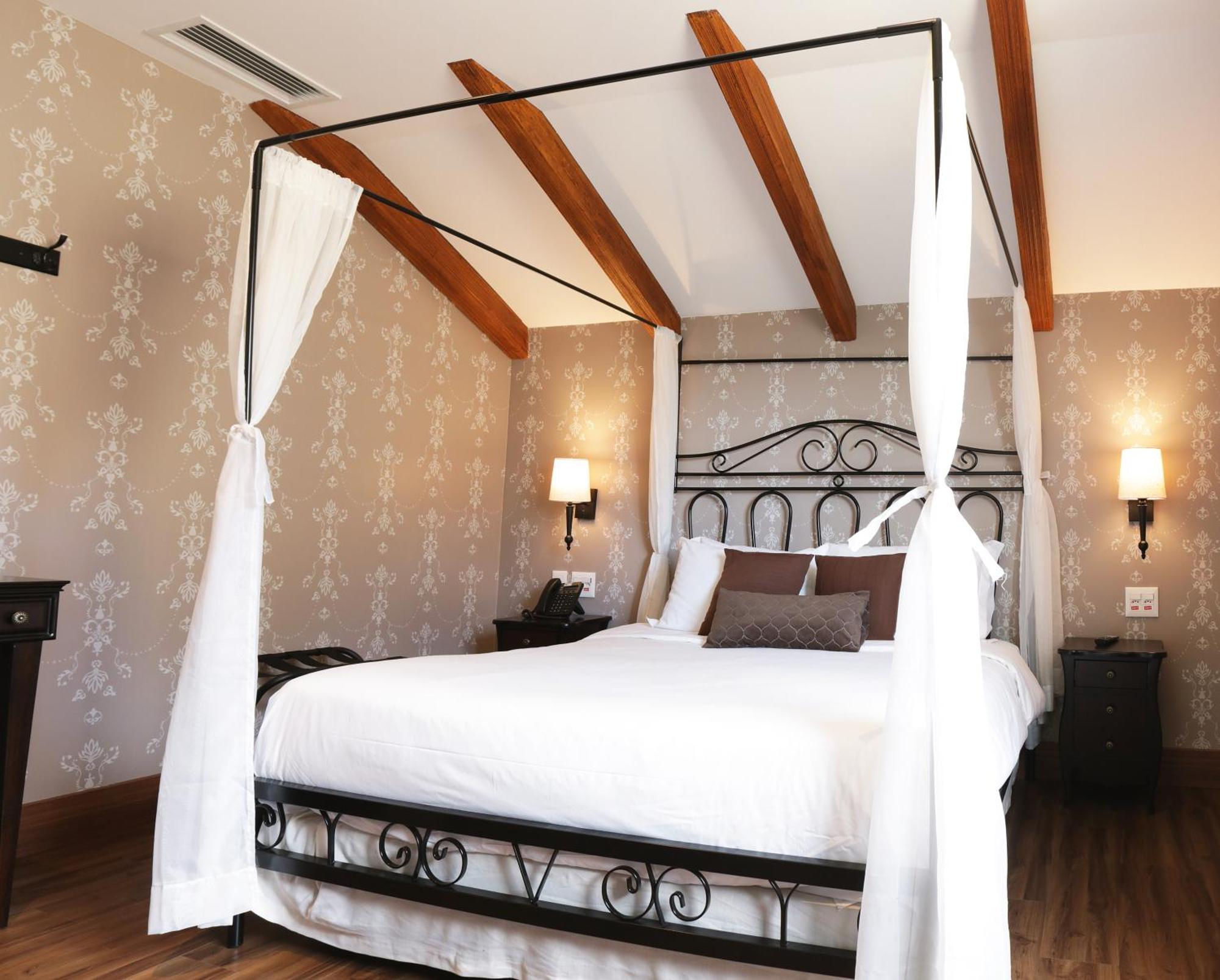 Buona Vitta Gramado Resort & Spa By Gramado Parks Exterior foto The photo shows a beautifully designed bedroom featuring a four-poster bed with a metal frame and flowing white curtains. The bed is adorned with white bedding and brown decorative pillows. The room has wooden beams on the ceiling and is decorated wi
