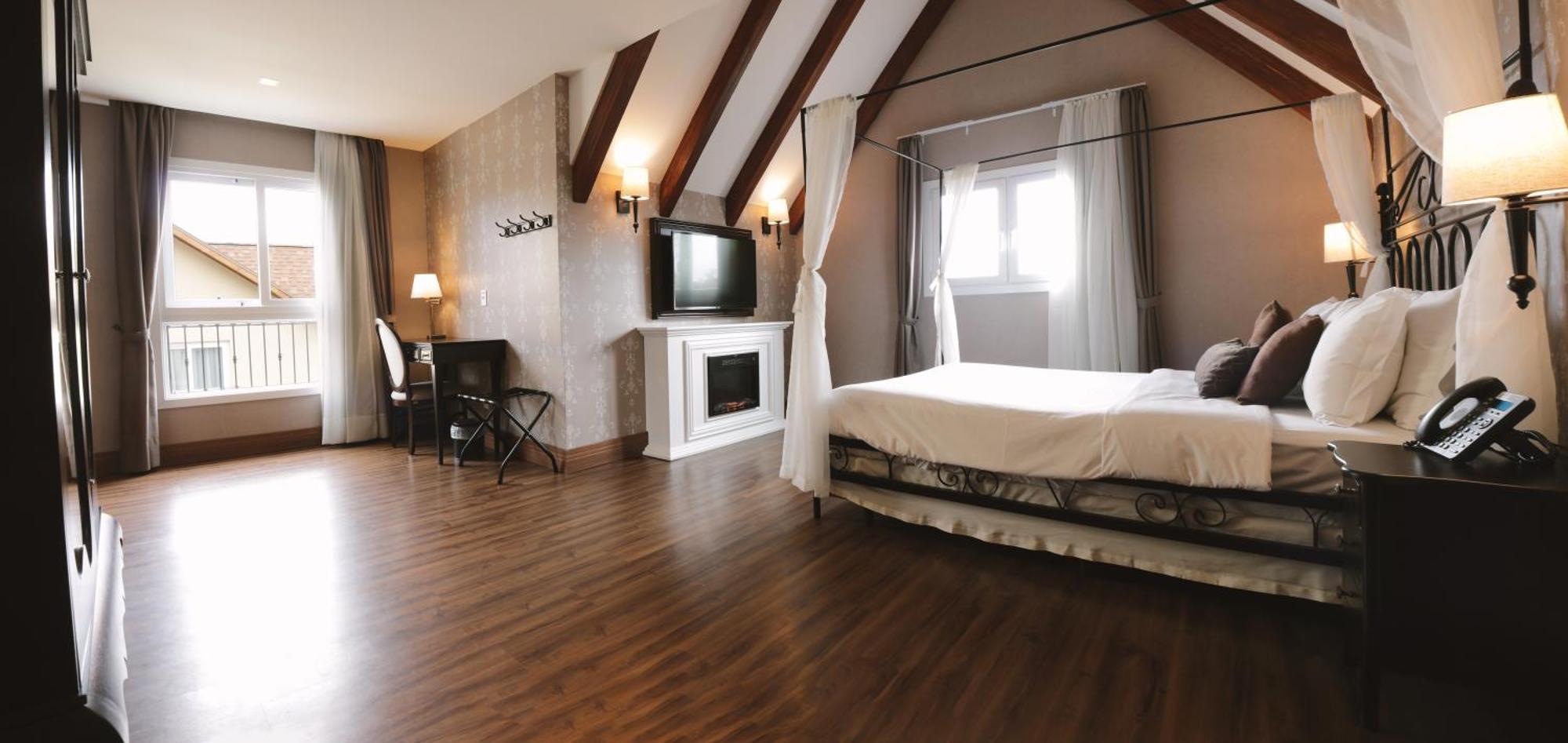 Buona Vitta Gramado Resort & Spa By Gramado Parks Exterior foto The photo shows a spacious hotel room with a modern and elegant design. There is a large bed with an overhead canopy, and the bed is dressed in white linens. To the side, there is a small seating area with a desk and chair. A flat-screen television i